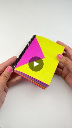 two hands holding a stack of brightly colored paper with a video playing button on it