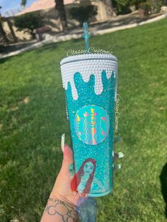 a person holding up a starbucks cup in their hand on the grass with palm trees behind them