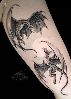 a black and white photo of two dragon tattoos on the leg, one with wings