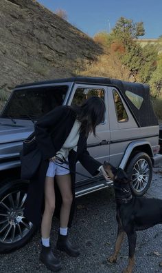 a woman is petting a dog in front of a car