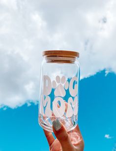 a person holding up a glass jar with the word dog mom on it in front of a blue sky