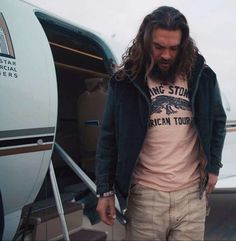 a man with long hair standing in front of an airplane