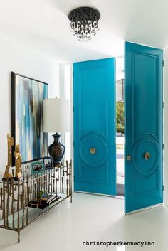 a blue door in a white room with a chandelier and painting on the wall