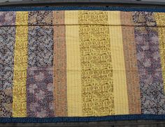 a yellow and blue patchwork quilt hanging on the side of a building