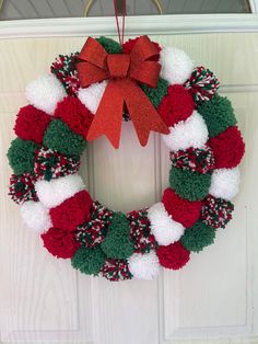 a red, white and green christmas wreath hanging on a door with a red bow