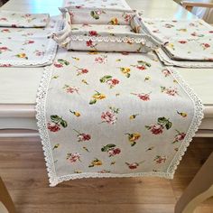 the table is covered with white linens and has flowers on it, along with lace trim