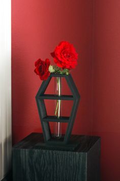 a vase with red flowers in it sitting on a black stand against a red wall