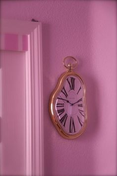 a clock mounted to the side of a pink wall next to a doorway and door