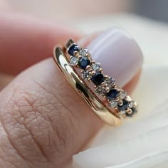 a woman's hand holding a gold ring with blue and white stones on it