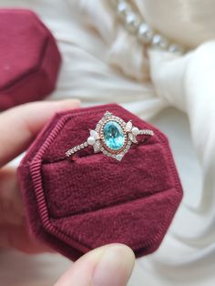 someone is holding an engagement ring in their red velvet gift box, which has a blue topaz surrounded by white diamonds