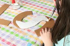 a girl is making letters out of cardboard on a table with a checkered table cloth