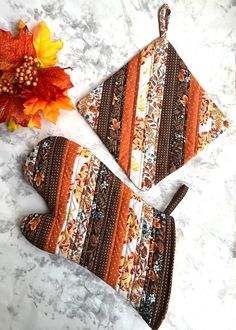 two oven mitts sitting on top of a counter next to a fall leaf and an orange flower