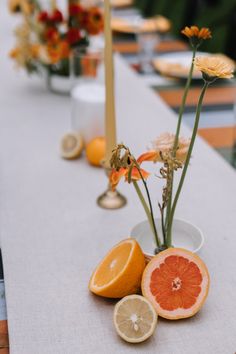 an arrangement of citrus fruits and flowers on a long table with silver candlesticks