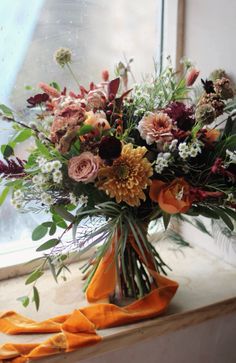 a vase filled with lots of flowers sitting on top of a window sill next to an orange ribbon