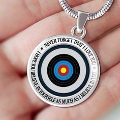 a hand holding a silver necklace with a target on it and the words never forget that love