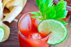 a close up of a drink on a wooden table with limes and cilantro