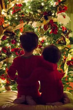 two children sitting in front of a christmas tree