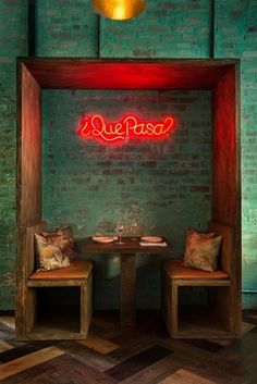 two chairs and a table in front of a brick wall with neon sign above it