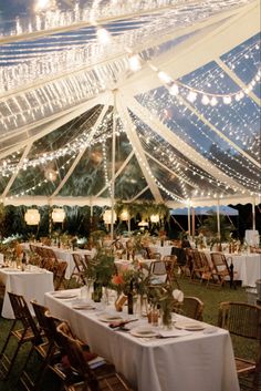 an outdoor tent with tables and chairs set up for a wedding reception in the evening