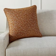 an orange and white pillow sitting on top of a beige couch next to a wall