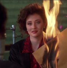 a woman holding a piece of paper in front of a fire and water fountain with flames coming out of it