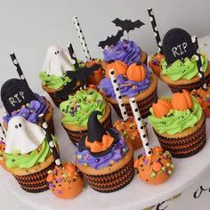 cupcakes decorated with green and purple frosting, topped with halloween decorations are sitting on a cake plate