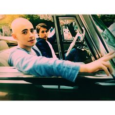 two men sitting in the driver's seat of a car with their hands on the steering wheel