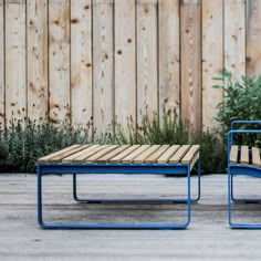 two wooden tables sitting next to each other on top of a cement floor near a fence