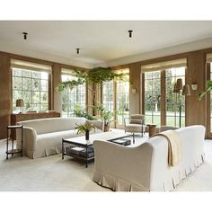 a living room filled with lots of furniture next to large window covered in plants and greenery