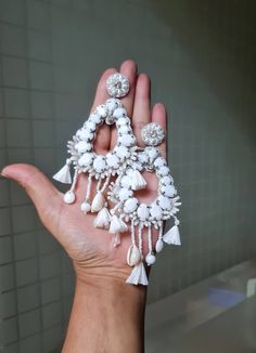 a hand holding several pieces of jewelry in it's palm, with white beads and tassels hanging from them