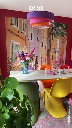 a dining room table with colorful chairs and flowers in a vase on the table next to it