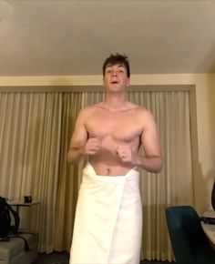 a shirtless man in a hotel room with his towel wrapped around his waist and looking at the camera