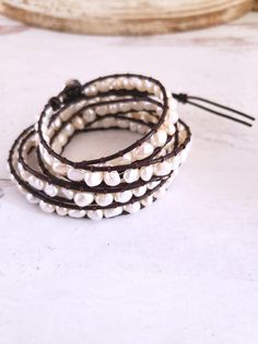 Beautiful genuine freshwater pearls are woven into these always on-trend leather pearl wrap bracelets. Wearing one of these bracelets will make you feel casually elegant since the pearls give a classy look to a traditionally bohemian style wrap bracelet. Choose from white pearls on natural tan leather or white pearls on dark brown leather. This pearl bracelet wraps around the wrist 5 times and is adjustable closure for flexible sizing. Bracelets are approximately 37 inches long and are adjustabl Chic Adjustable Pearl Bracelet With Charm, Elegant Brown Wrap Bracelet As A Gift, Elegant Handmade Leather Bracelet, Chic Adjustable Pearl Bracelet With Pearl Charm, Elegant Handmade Adjustable Leather Bracelet, Elegant Beaded Leather Bracelet Gift, Elegant Adjustable Hand Wrapped Bracelet, Elegant Hand Wrapped Leather Bracelet, Elegant Hand Wrapped Leather Bracelet Gift