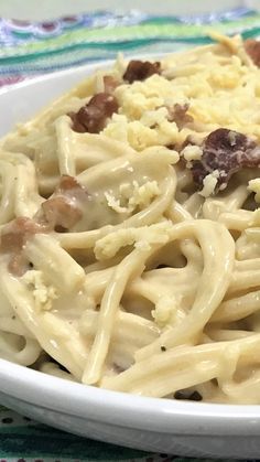 a white bowl filled with pasta and meat on top of a colorful table cloth next to a fork