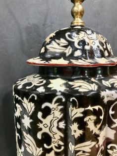 a black and white ceramic covered jar with a gold top sitting on a wooden table