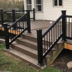 a wooden deck with black railing and handrails next to a white house in the background