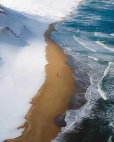 an aerial view of the beach and ocean with snow covered mountains in the back ground