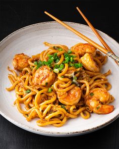 a white plate topped with noodles and shrimp next to chopsticks on a table