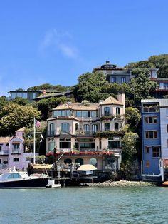 several houses on the side of a hill next to water with boats parked in front of them