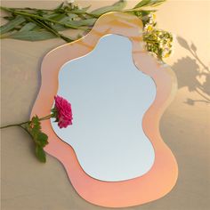 a mirror sitting on top of a table next to a pink rose and green leaves