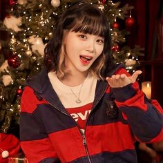 a young woman standing in front of a christmas tree holding her hand up to the camera