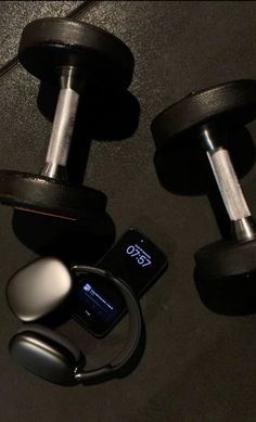 two dumbbells, an mp3 player and earphones on a black surface