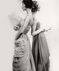 two women in evening dresses looking at each other's back with angel wings on their shoulders