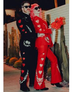 a man and woman dressed up in red clothing posing for a photo with cacti behind them