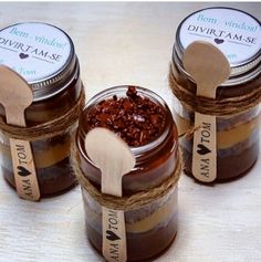 three jars filled with different types of food on top of a wooden table next to two spoons