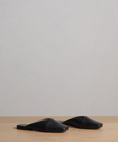 a pair of black slippers sitting on top of a wooden floor next to a white wall