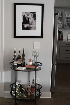 a bar cart with bottles and glasses on it in front of a framed photo above the bar