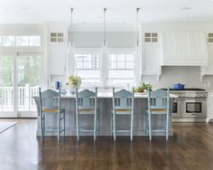 a kitchen with white cabinets and blue chairs at the center of the room is an island