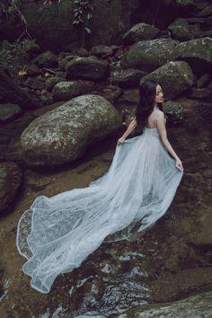 a woman in a white dress standing on rocks