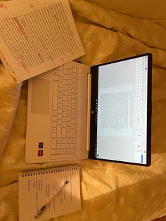 an open laptop computer sitting on top of a bed next to a notebook and pen